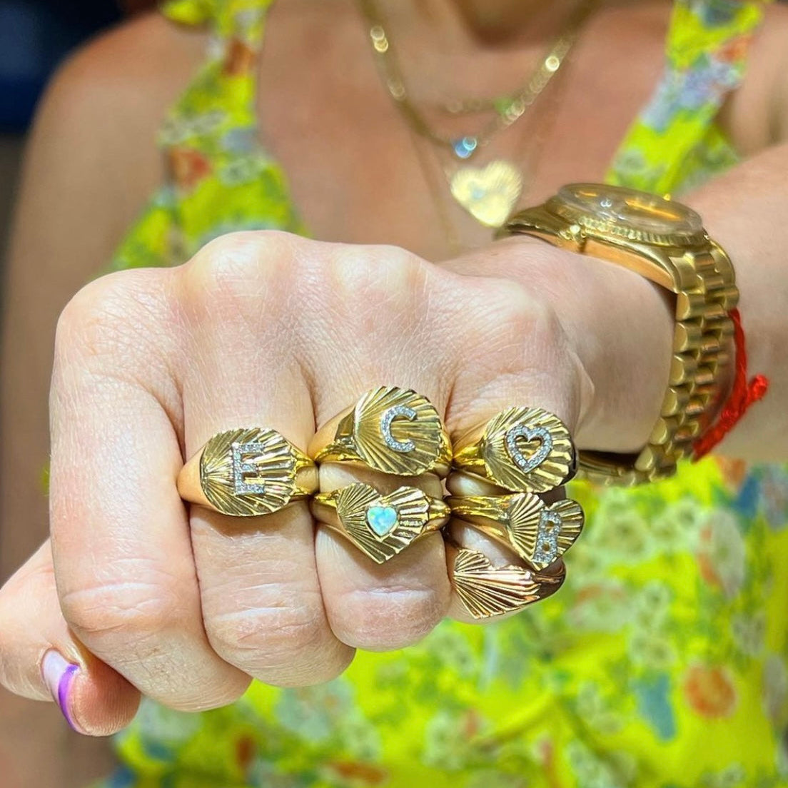 Wide band fluted yellow gold signet ring with diamond initial shown on hand with other fluted and diamond rings