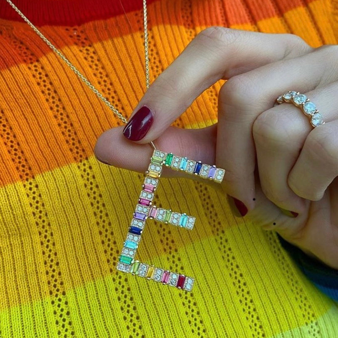 Jumbo yellow gold initial necklace with rainbow baguettes shown as a bold statement piece on a neck