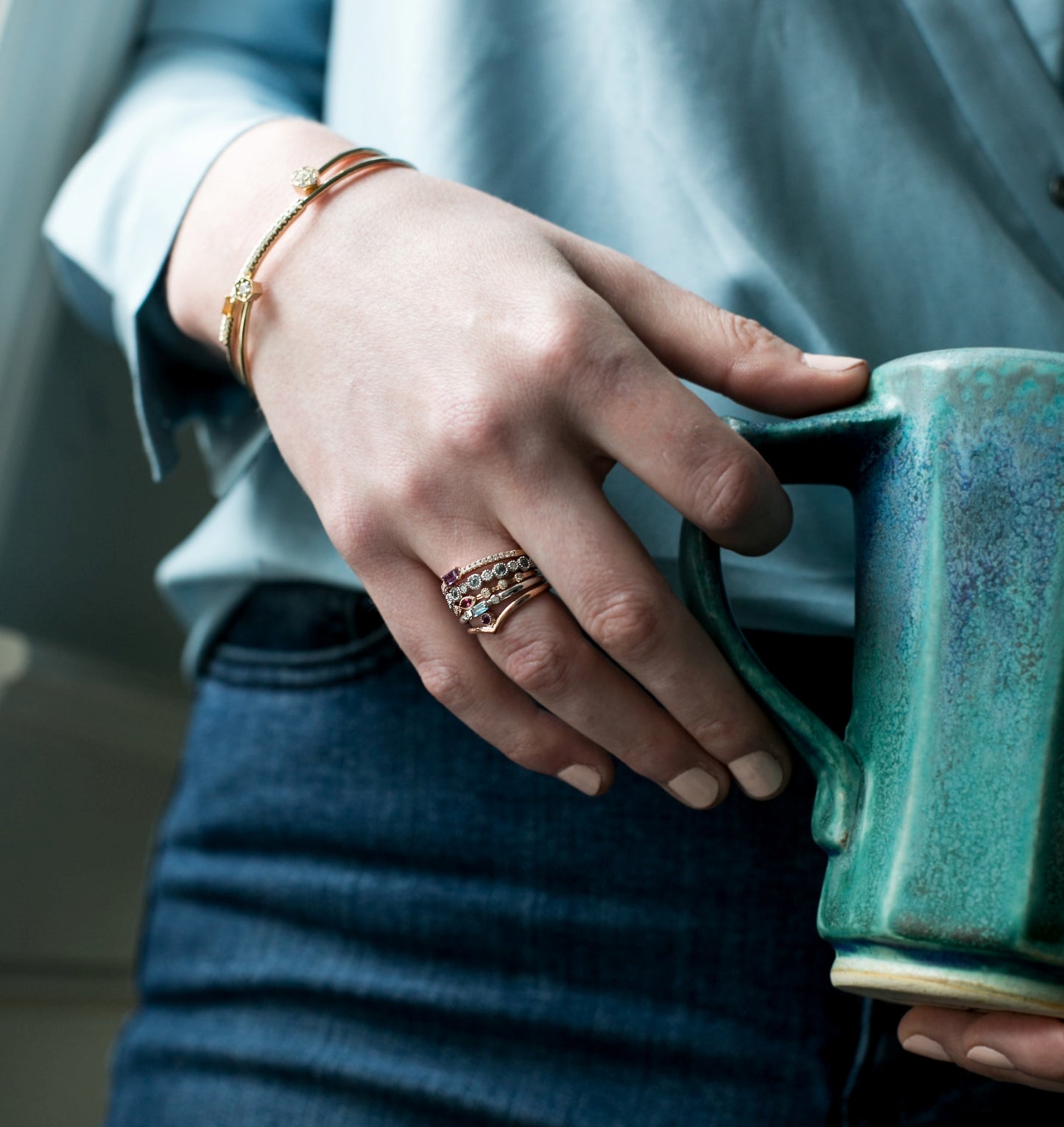 Thin banned gold ring with round diamonds shown on finger with denim