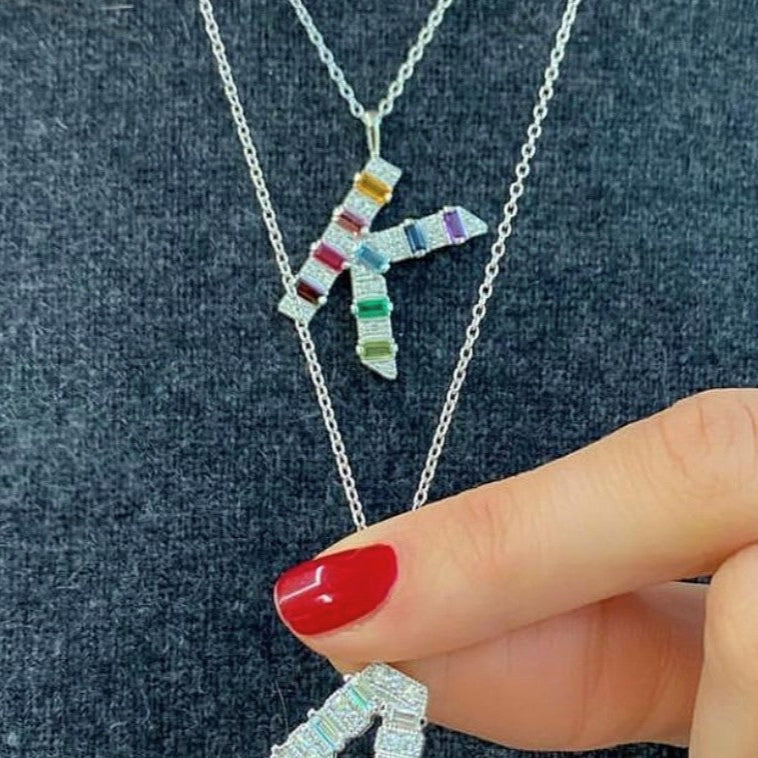 Mini white gold initial necklace with rainbow baguettes and round diamonds shown layered perfectly on the neck