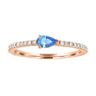 Rose gold skinny band with a pear shaped blue topaz in the center and round diamonds on the shank.