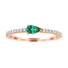 Rose gold skinny band with a pear shaped emerald in the center and round diamonds on the shank.