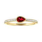 Yellow gold skinny band with a bezeled pear shape garnet in the center and round diamonds on the shank.