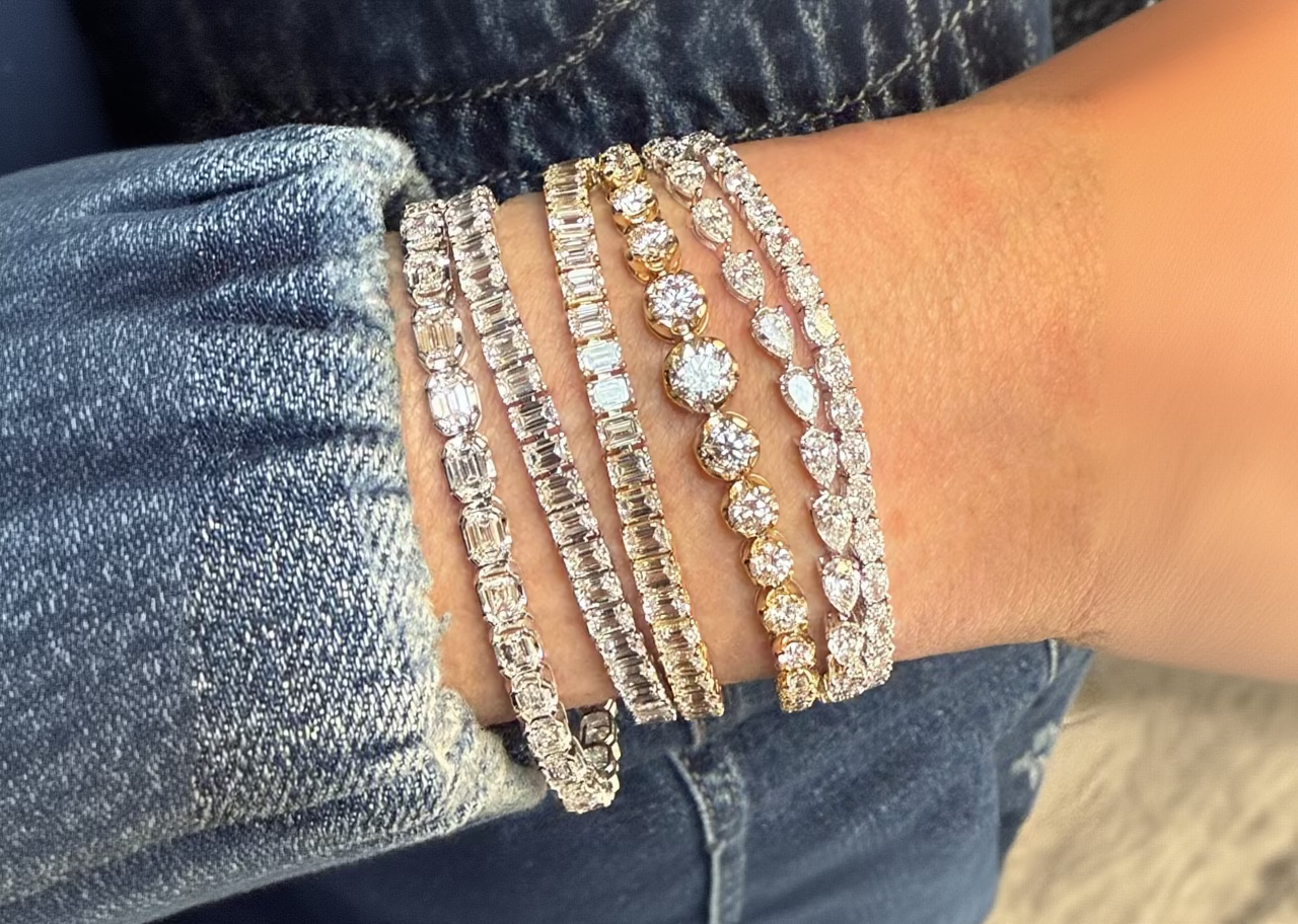 Close-up of a wrist wearing multiple diamond bracelets on a denim background