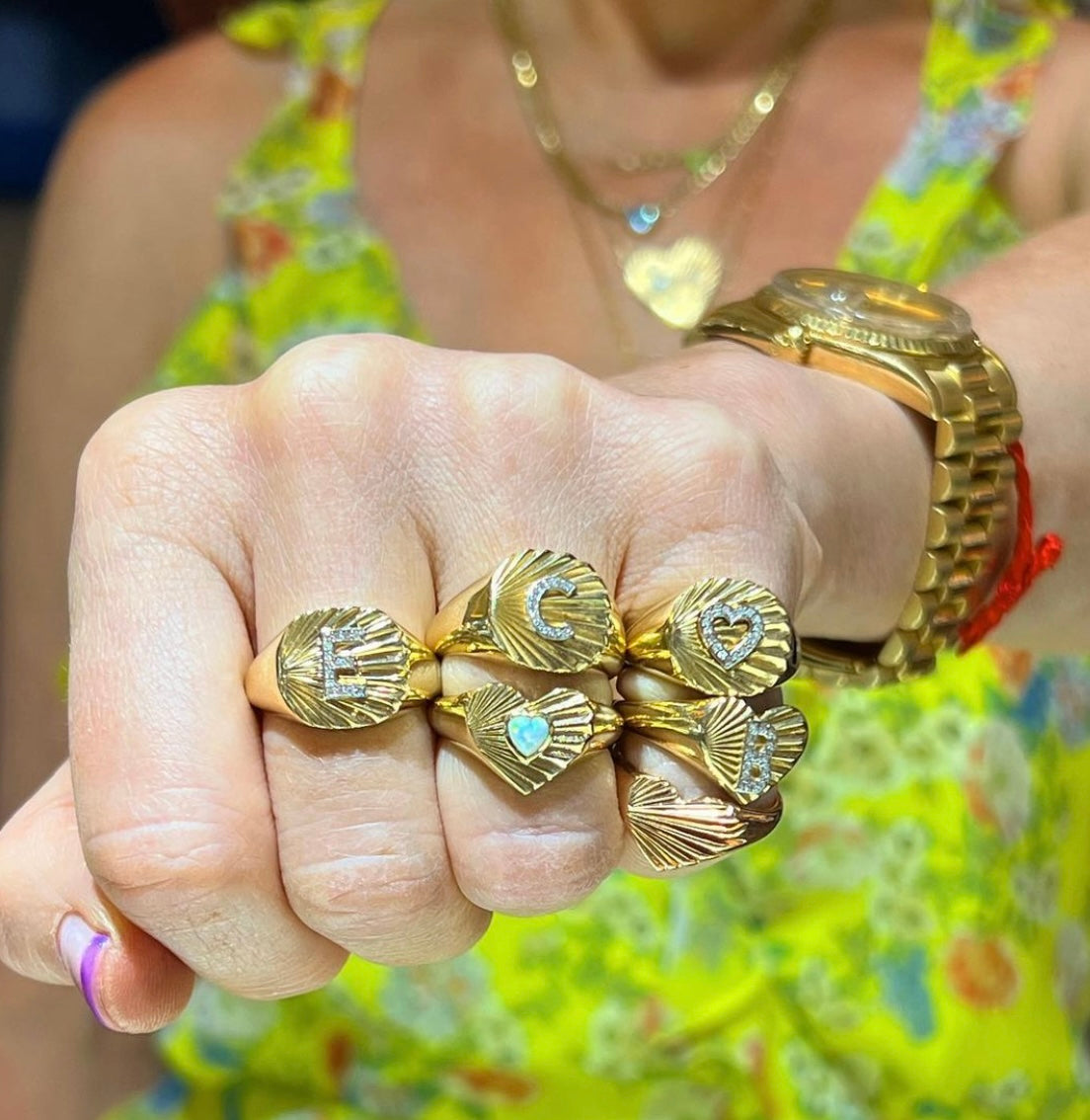 Wide band fluted yellow gold signet ring with diamond initial shown on hand with other fluted and diamond rings