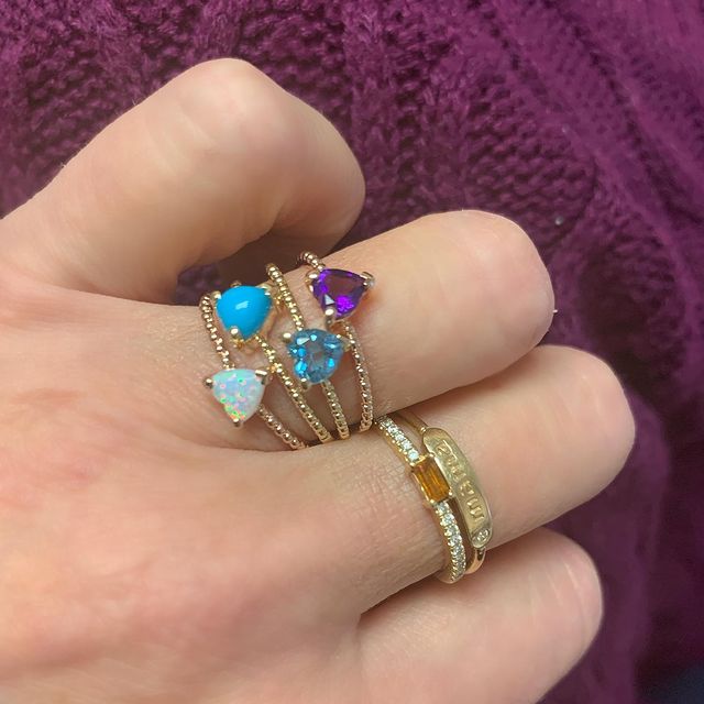Thin banned gold ring with heart shaped gemstones layered on finger
