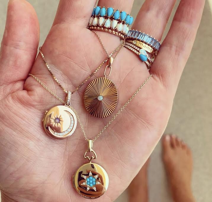 Rose gold pleated oval locket with round opal in center shown with other lockets 