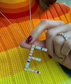 Jumbo yellow gold initial necklace with rainbow baguettes shown as a bold statement piece on a neck